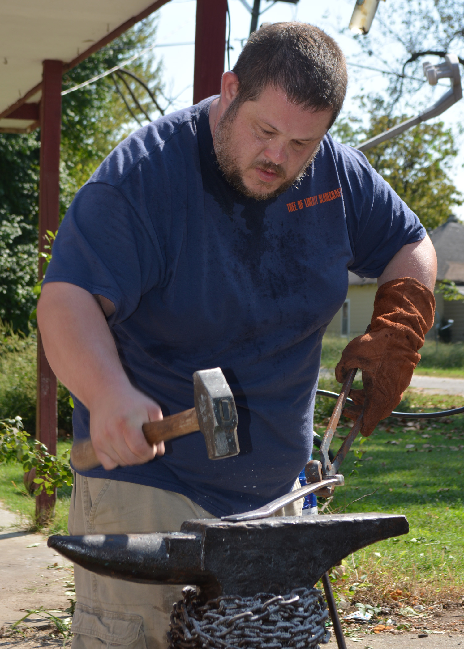 A man hammers a metal item on an anvil.