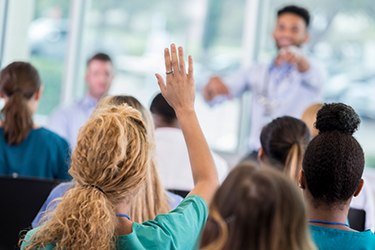 classroom01 Unrecognizable female nurse raises hand to ask a question during medical conference. The conference speaker is pointing at her.