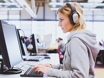 adult education, student in headphones working on computer in the library or classroom of university