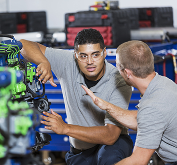 externships04 Two multi-ethnic young men in vocational school, taking a class on reparing diesel engines. They are working on an engine that has had parts painted different colors for training purposes. They are wearing safety glasses.