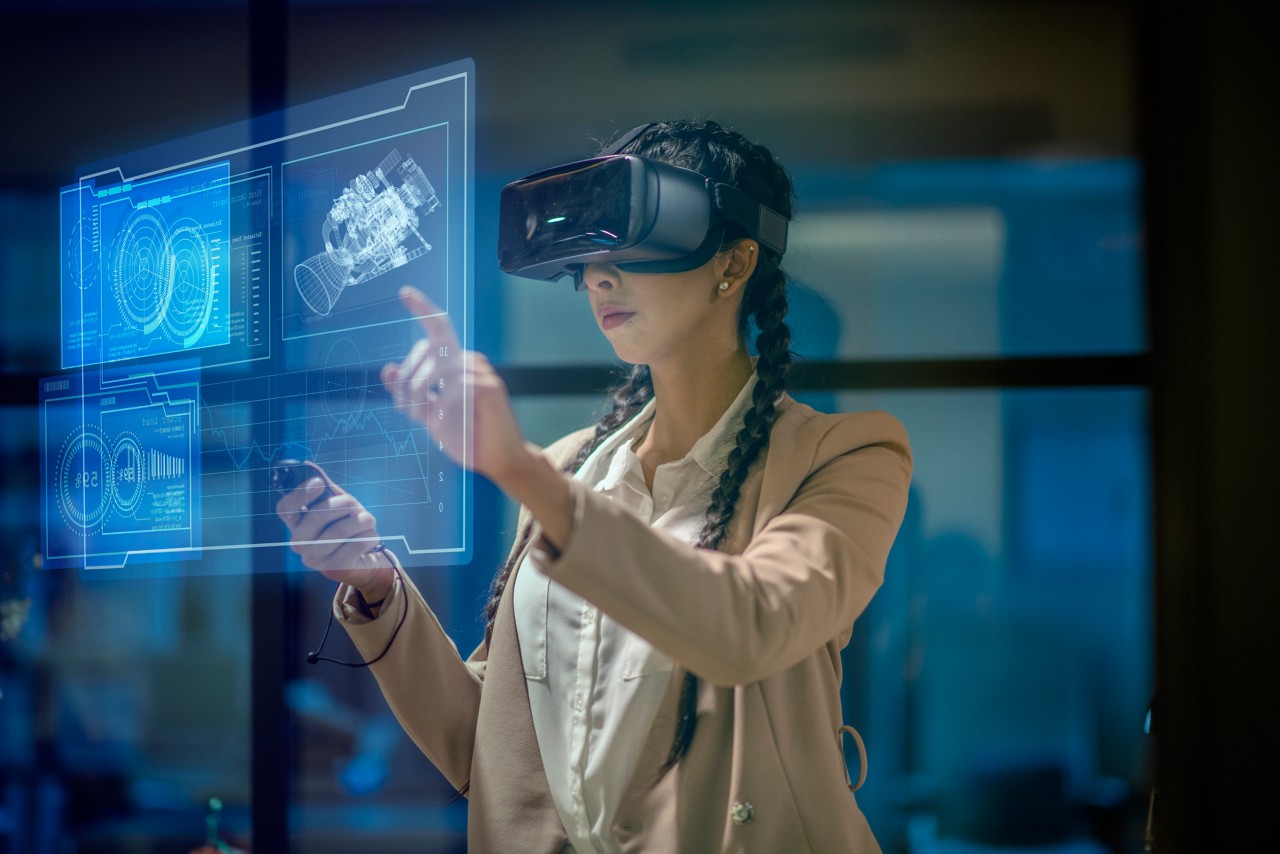 Getty Images #1305158903 of a female engineer wearing a virtual reality headset at work to explore an upcoming mechanical engineering project. She uses her hands to manipulate and explore the finer details.