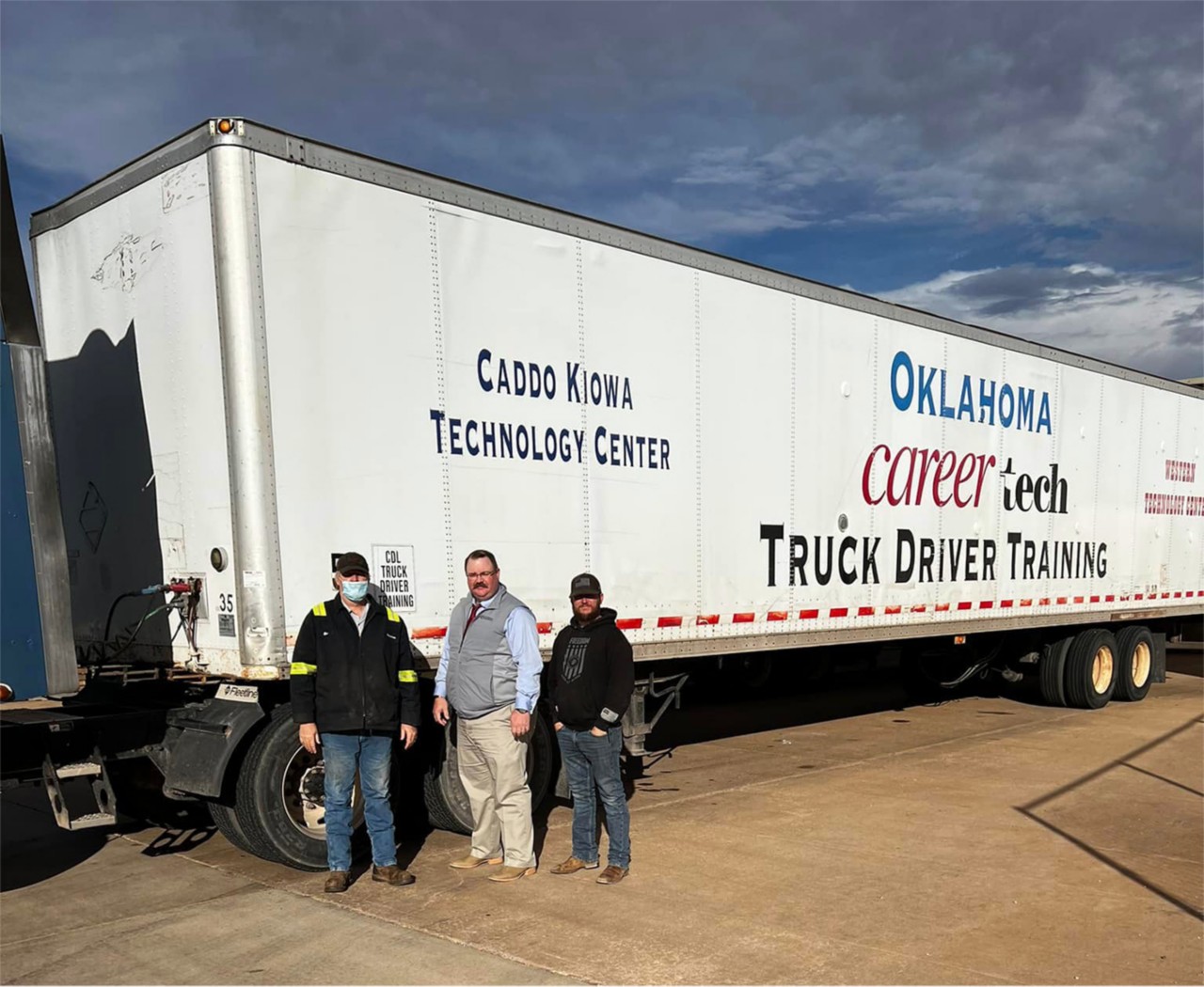 Three men stand in front of the trailer Caddo Kiowa Technology Center donated for transporting clothing donations to the VA.