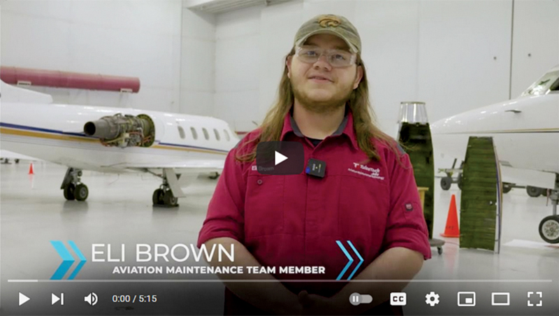 Eli Brown, Tulsa Tech aviation maintenance team member, stands in an airplane hangar in front of two airplanes. Link opens YouTube video in new tab.