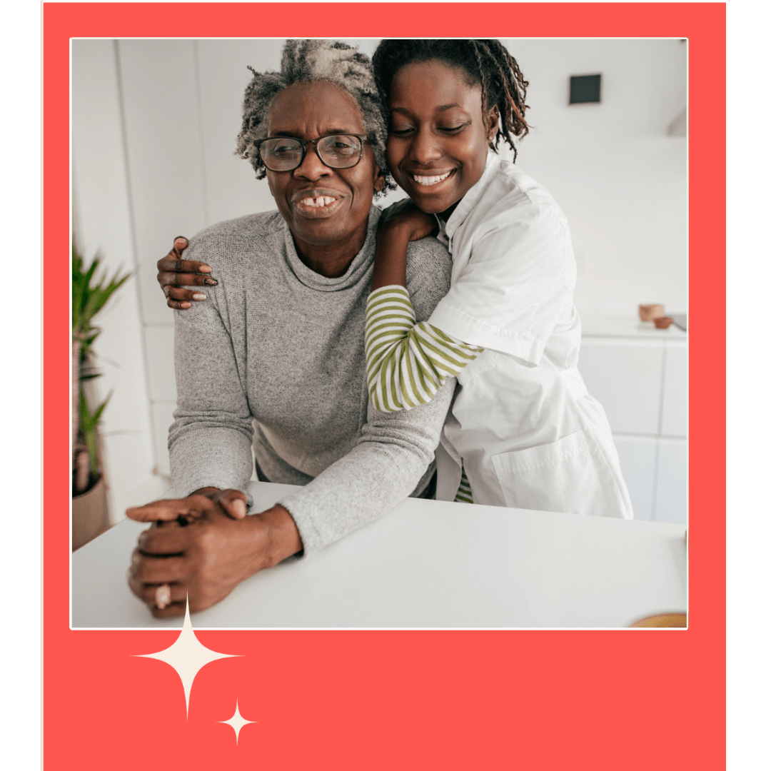 Two Black women in a kitchen. The older woman is leaning on the counter and the younger women is hugging her.