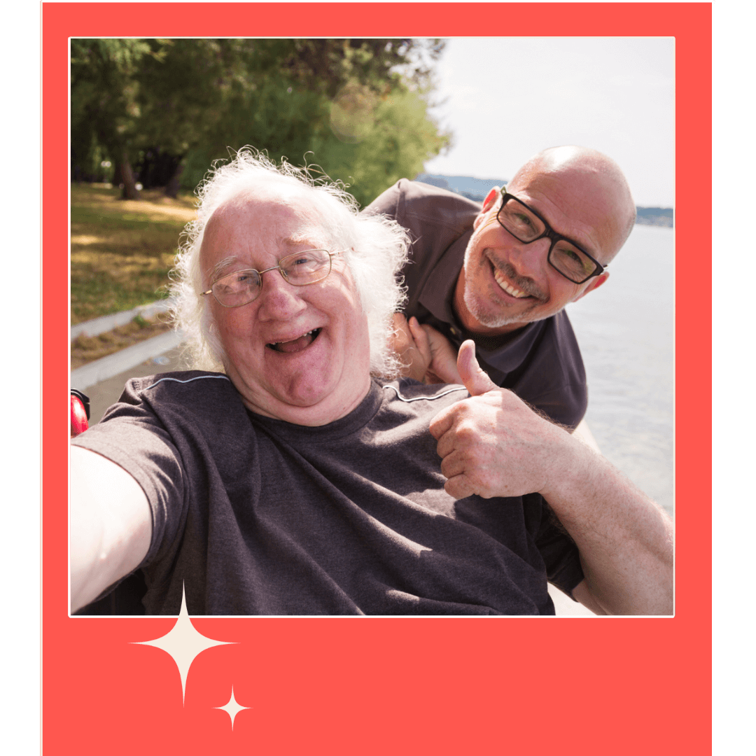 Two men smiling. Both men are wearing glasses. One man is older, has white hair and is in a wheelchair.