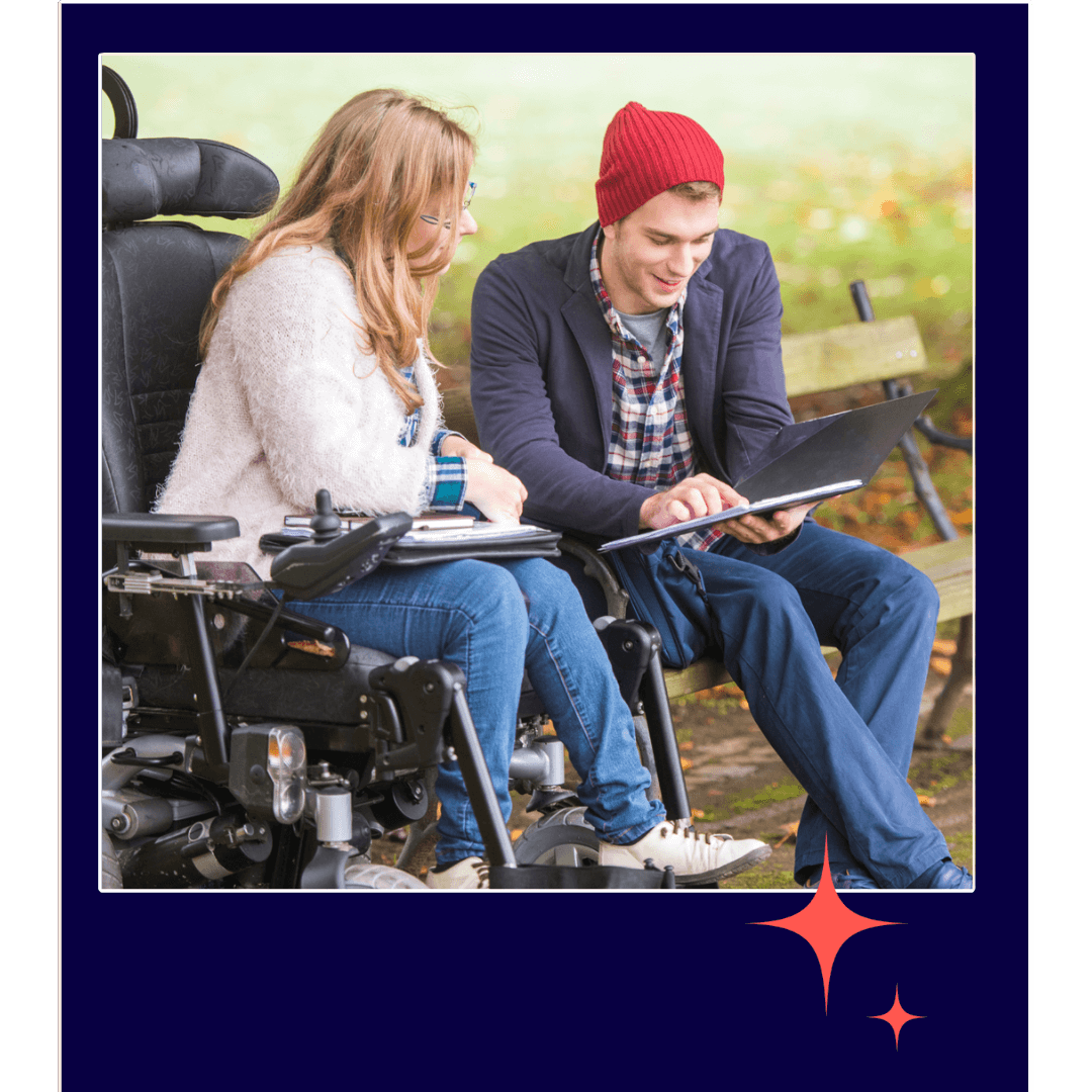 Man and woman looking at an iPad. The woman is in a wheelchair. The man is sitting on a park bench.