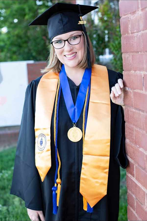 Kaydee Clark poses next to a brick wall in her graduation cap and gown.