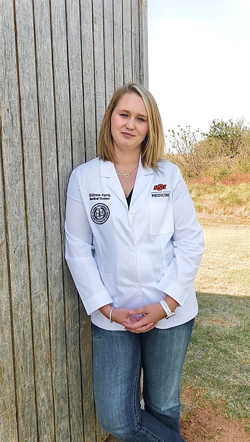 ShiAnne Farris wears her OSU School of Medicine white coat and leans against a building.