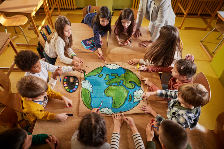 Group of young children around a table with colored drawing of Earth in middle.