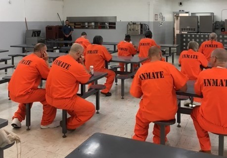 Inmates in facility cafeteria wearing orange uniforms.