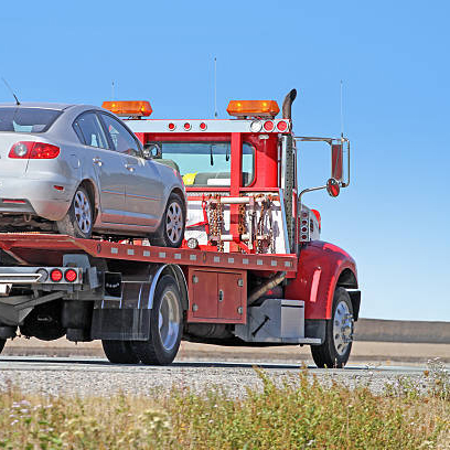 Rear quarter view of a red tilt bed tow truck on a highway carrying a nondescript vehicle.