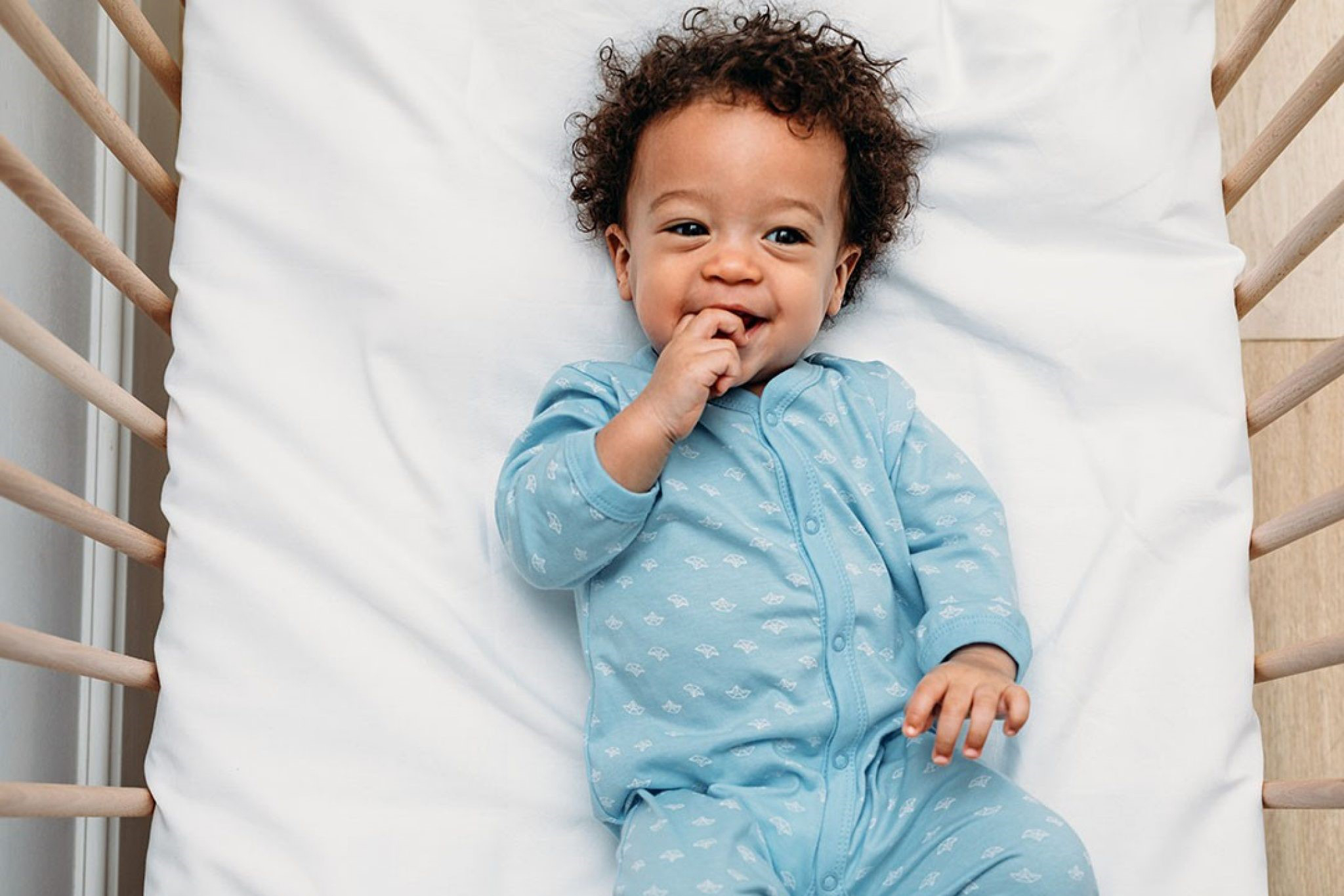 Overhead view of a happy baby boy lying in a crib wearing pajamas