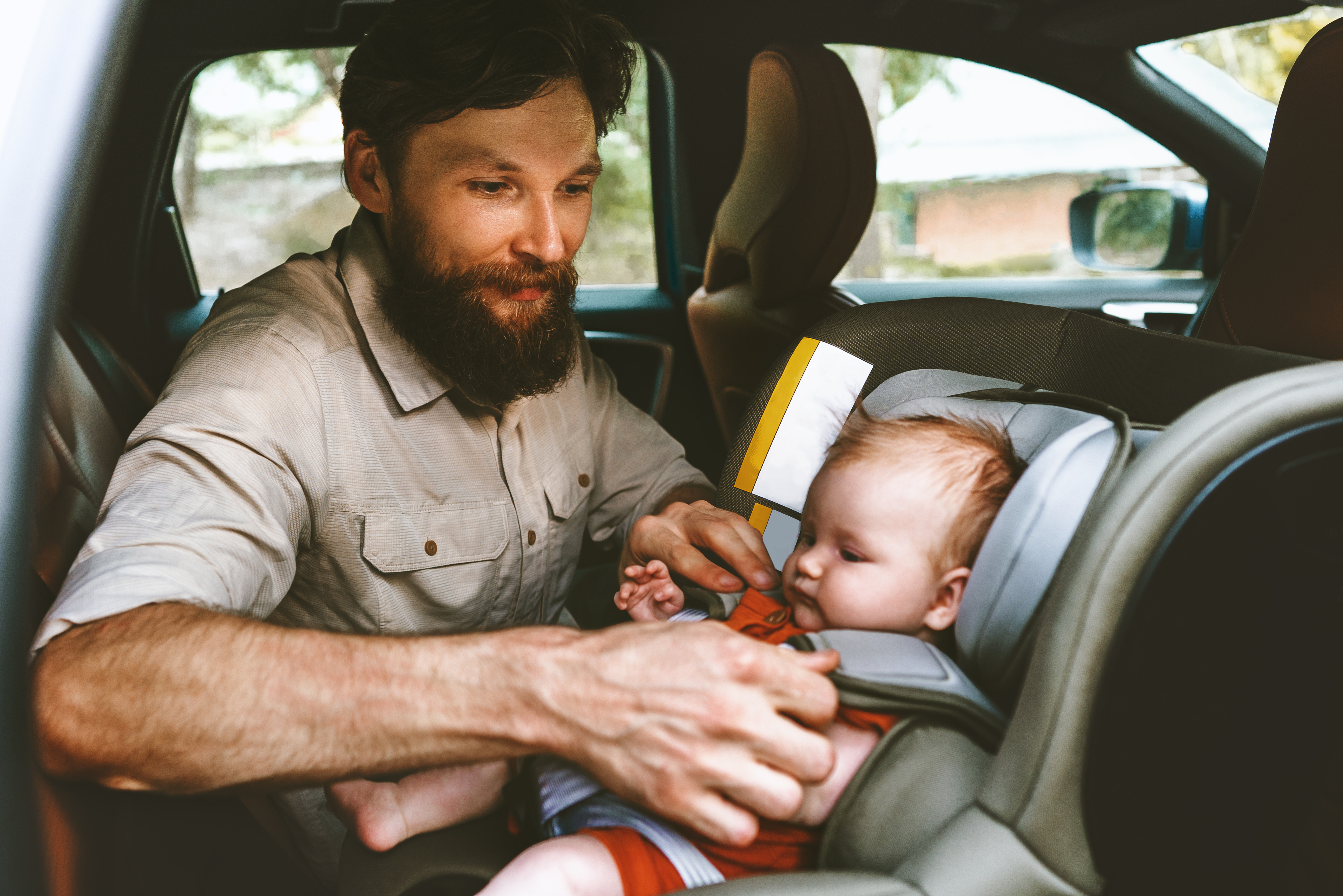 Father putting baby in safety car seat happy family vacation road trip lifestyle child care transportation rear-facing