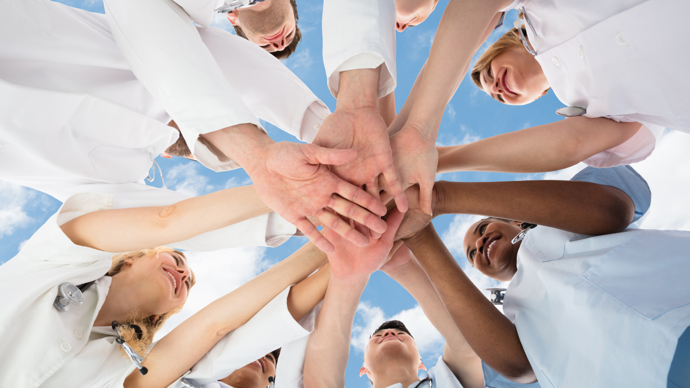 A group of nurses standing in a circle with all of their hands laid on top of each other.