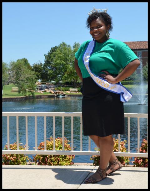 Thompson poses with crown and shash in front of a water feature