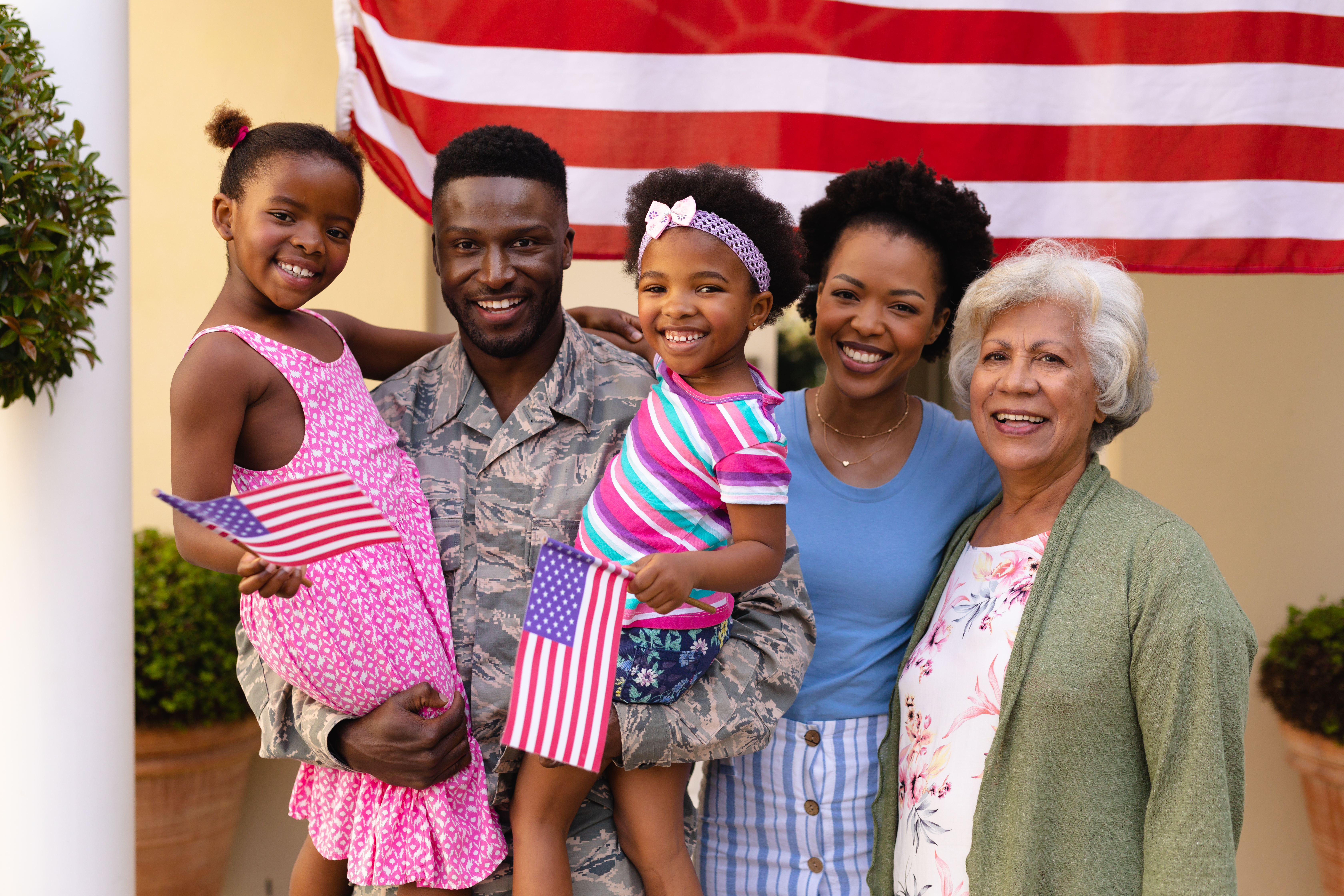 Portrait of smiling african american family with army father carrying daughters at entrance