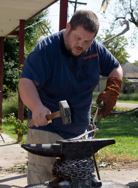 A man with a hammer beats a strip of metal on the anvil.