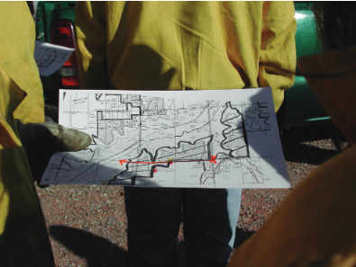 Two fire crew members overseeing a controlled low-intensity prescribed burn, with flames and smoke visible.