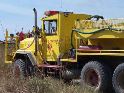Large fire management truck driving on a grassy field during a prescribed burn, helping control and manage the fire.