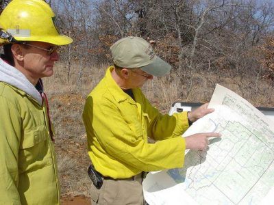 Person using a weather station on a grassy field to check wind and weather conditions before a prescribed burn.