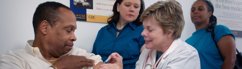 Man receiving injection from nurse while two other caretakers look on