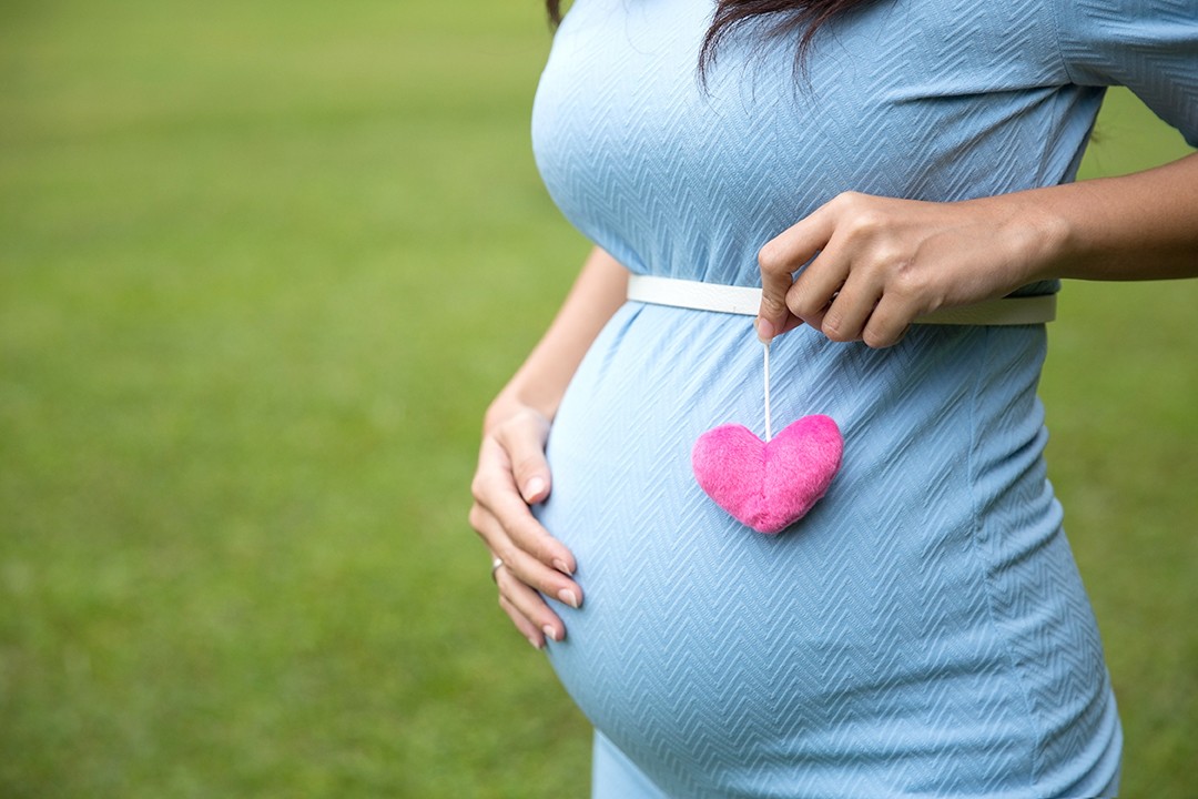 A portrait of a pregnant woman in blue dress holding a single heart shape accessories