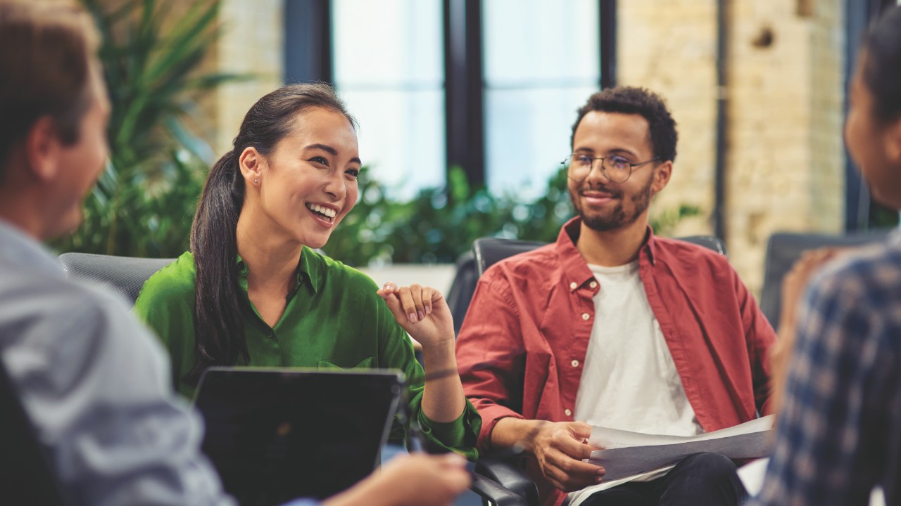 People gathered around having a meeting with laptops and notpads.