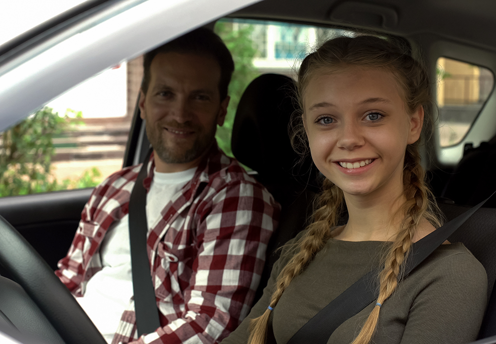 Happy female smiling into camera, sitting in car with instructor, driving school