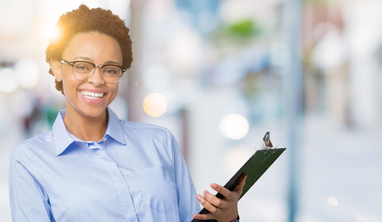 Young african american businesss woman holding clipboard over isolated background with a happy face standing and smiling with a confident smile showing teeth