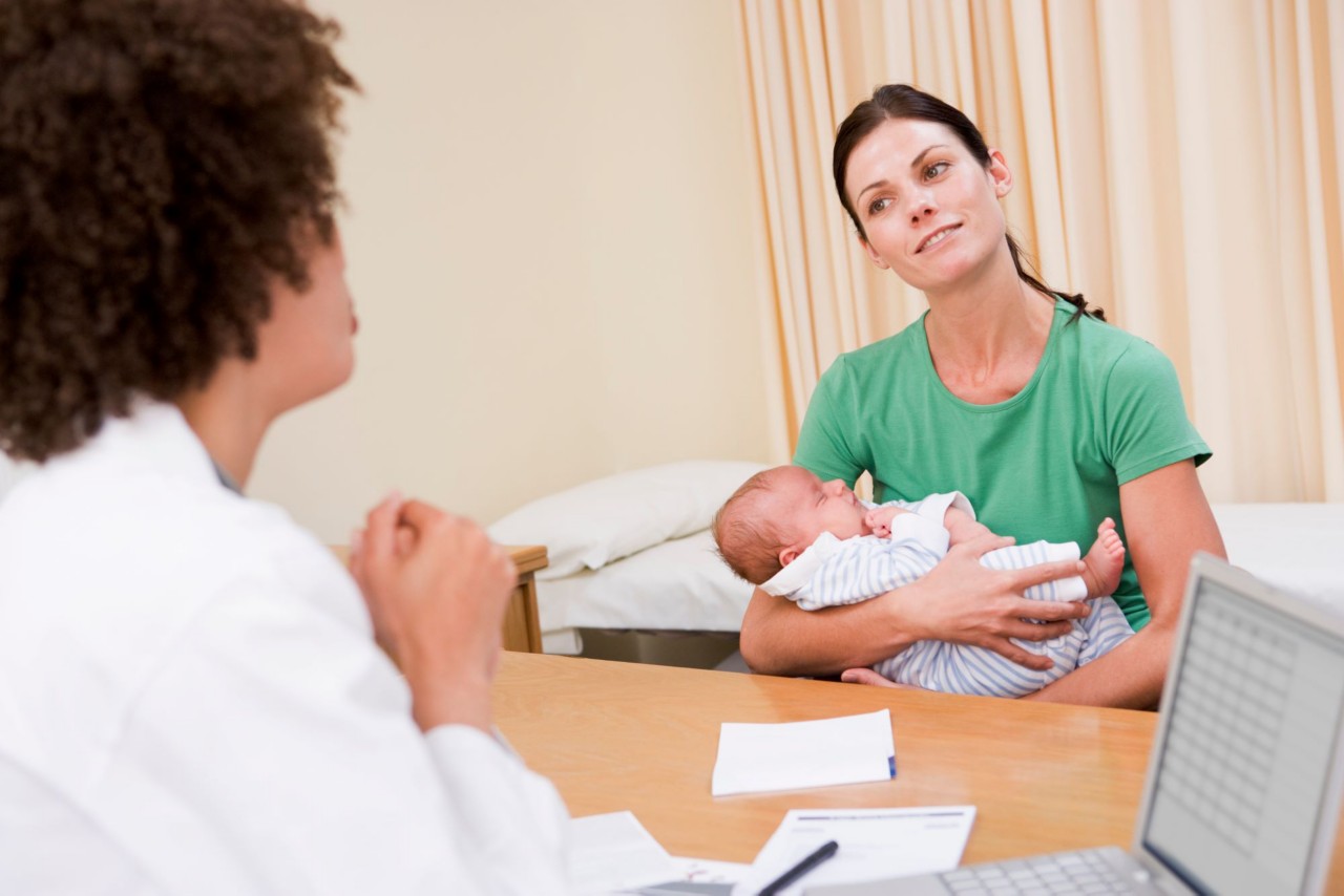 A woman holding a baby talks with a clinician.