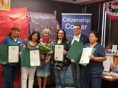 New citizens holding certificates standing in from of banner