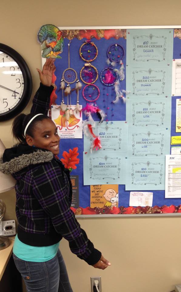 Teen girl showing off a bulletin board covered with literacy / reading awards.