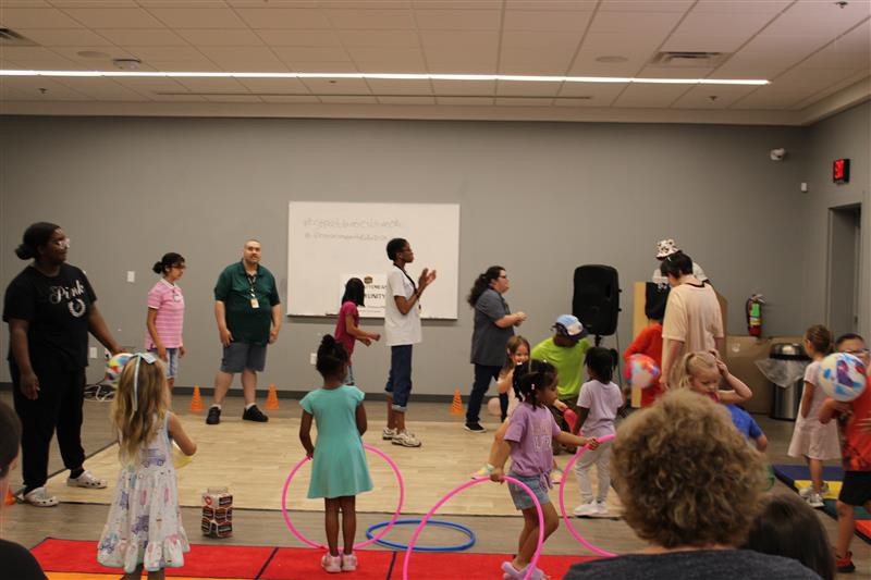 A group of children and adults enjoying activites at the library like hula-hooping and playing with baloons 