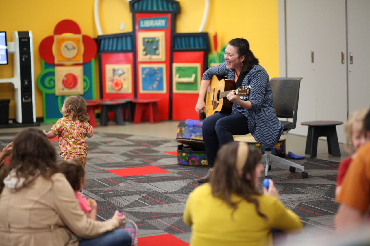 A librarian playing guitar and singing with children and the library