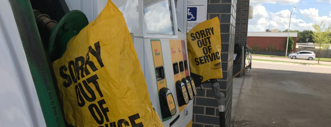 A closeup photo of diesel fuel pumps with a yellow plastic bag around the handle that reads, "sorry out of service," with a gas station in the background