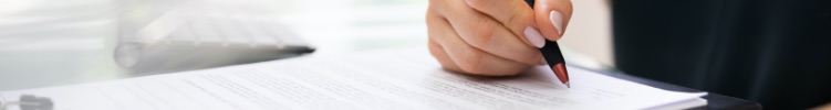 Hand using a pen to write on paper that is sitting on a flat surface