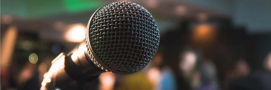 Public comments A close-up of a microphone in a microphone stand with blurry background including people outside at an event.