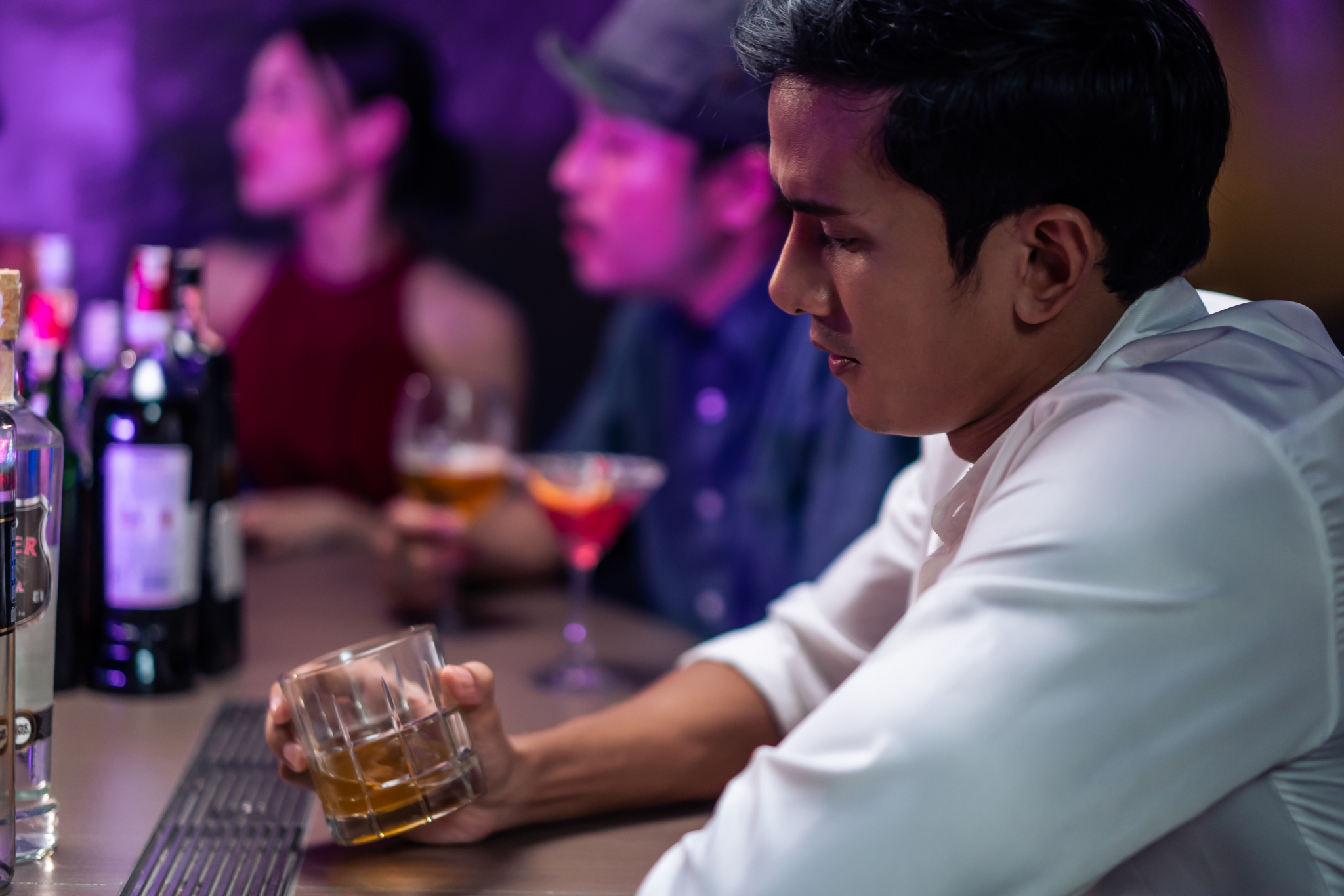 Asian depression man feeling heart broken and drinking beer in a bar. Attractive male sitting on counter bar, holding a bottle of alcohol feeling loneliness, drunk and hangover alone at night club. Asian depression man feeling heart broken and drinking beer in a bar. Attractive male sitting on counter bar, holding a bottle of alcohol feeling loneliness, drunk and hangover alone at night club.