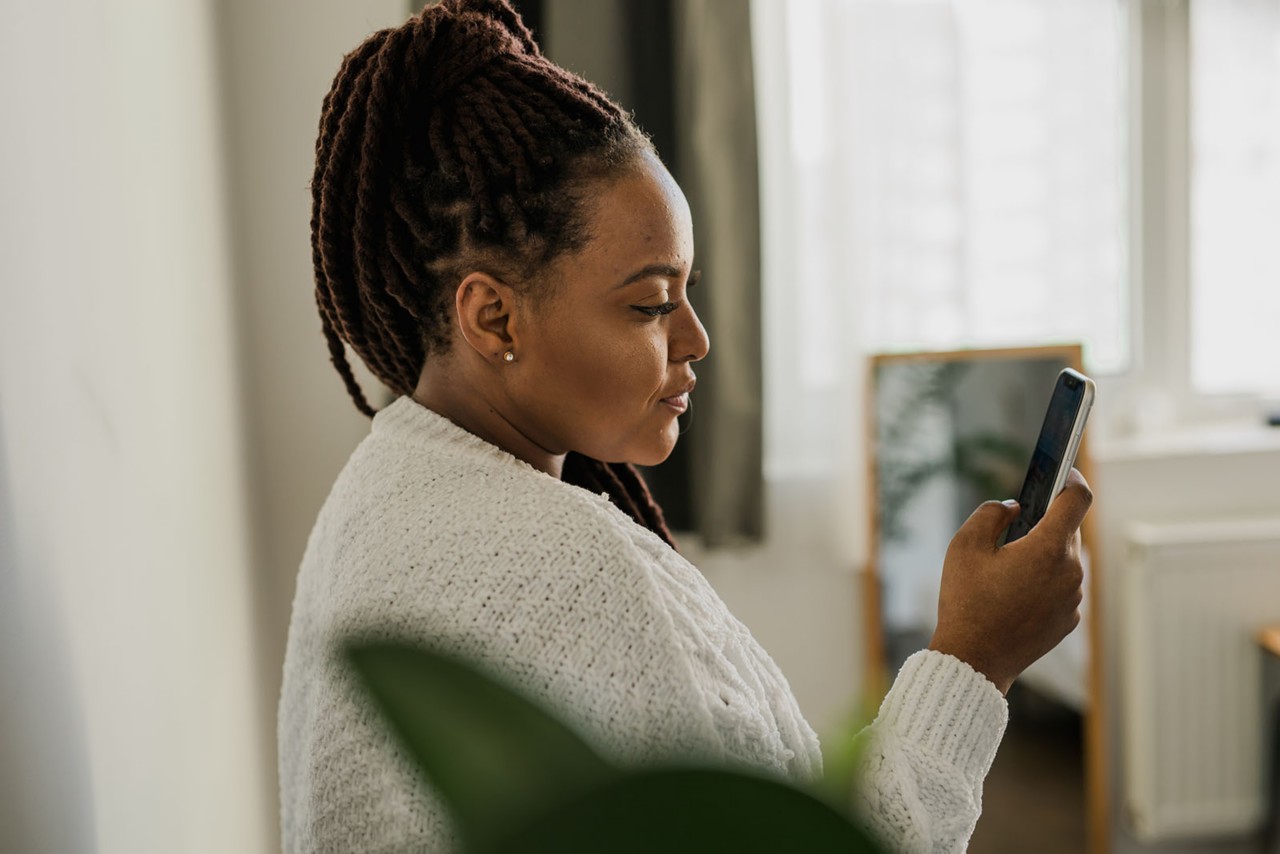Portrait of good-looking African female student dressed casually holding mobile phone and typing messages