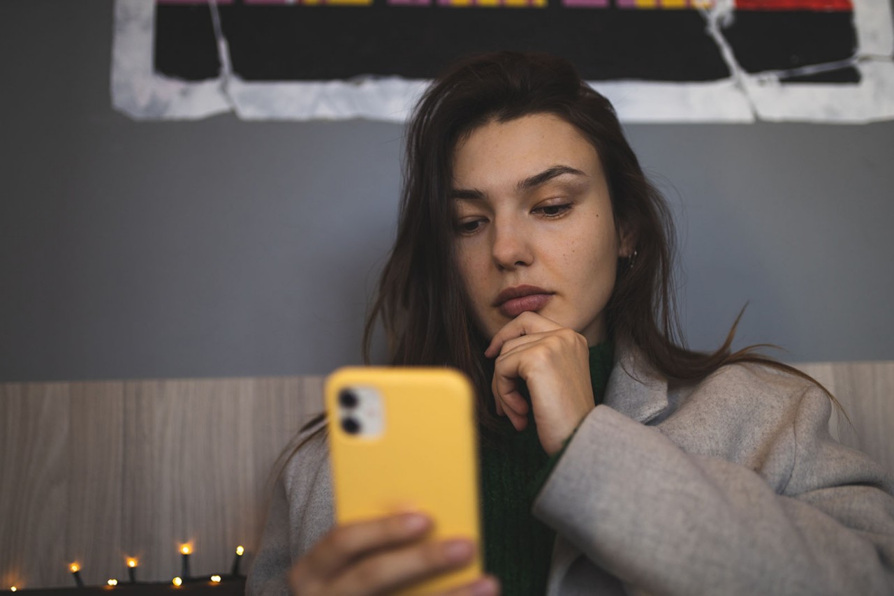 young woman sitting down looking at brightly colored mobile phone