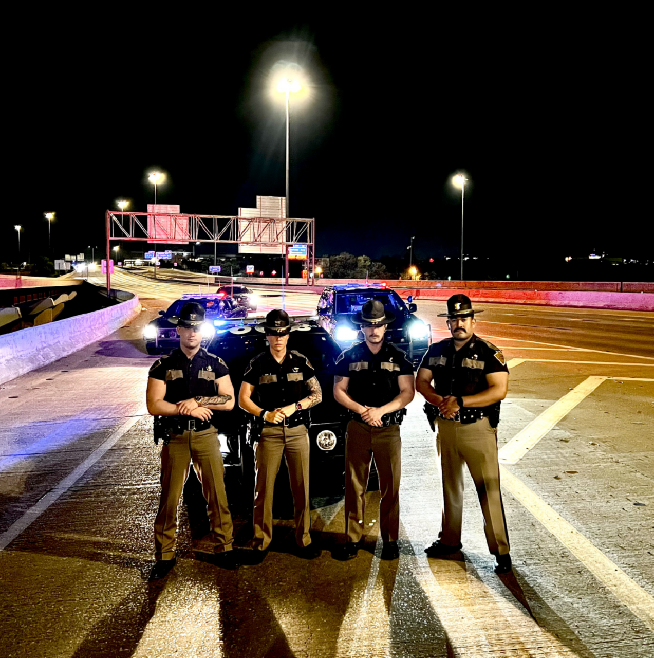 four ohp troopers standing together at night in front of their patrol cars