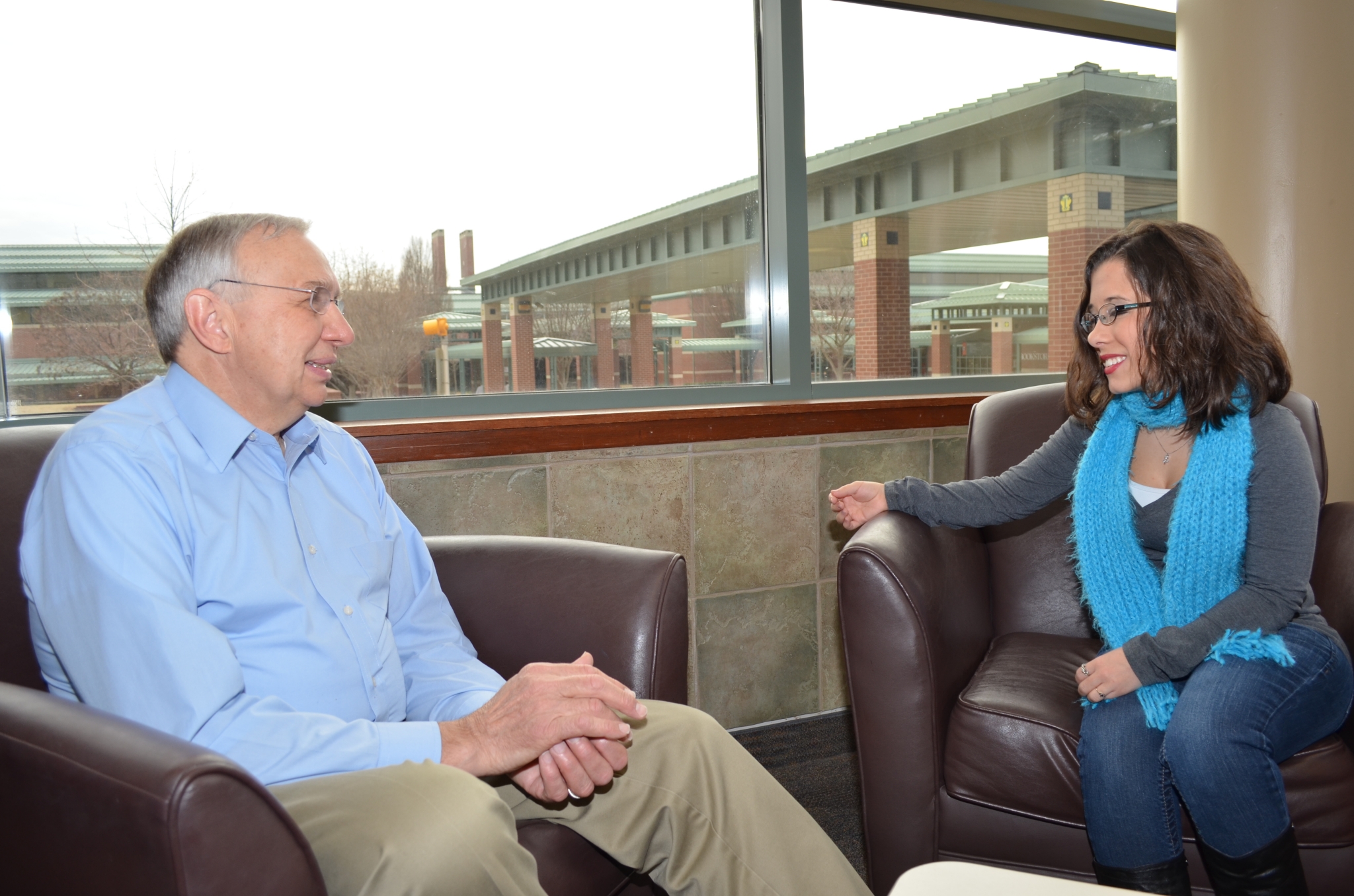 A man and a woman who is small stature chat in a sitting area. 
