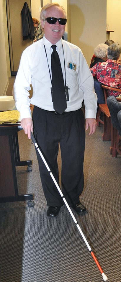 A man is walking with a white cane in an office.
