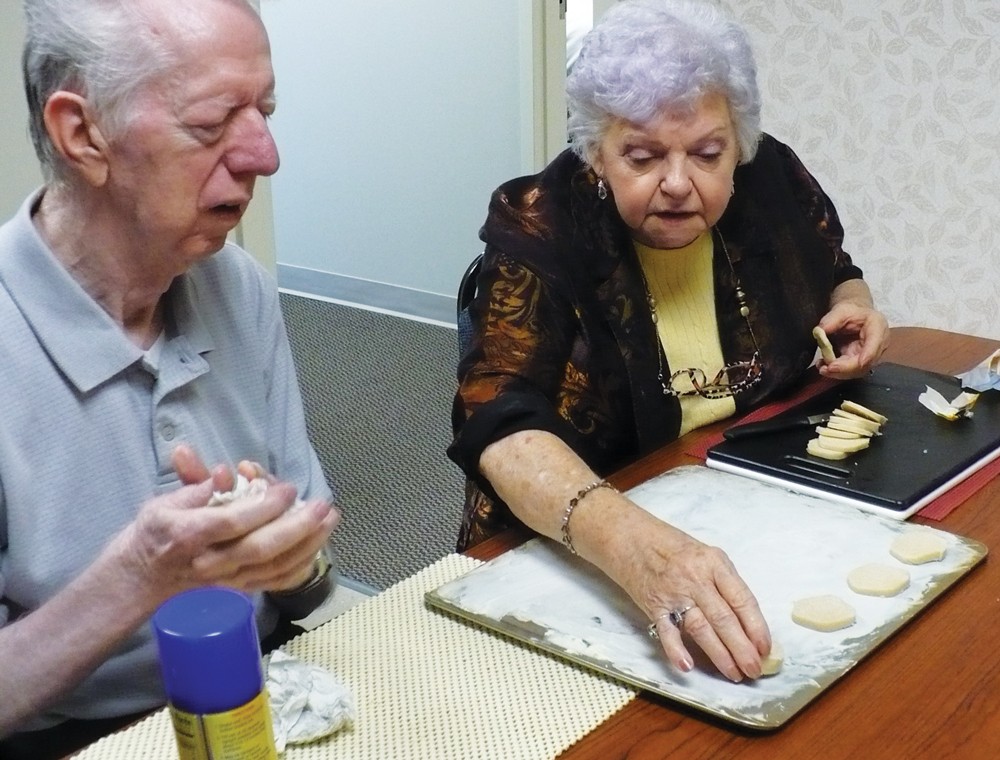 A older man and woman sitting at a table preparing cookies