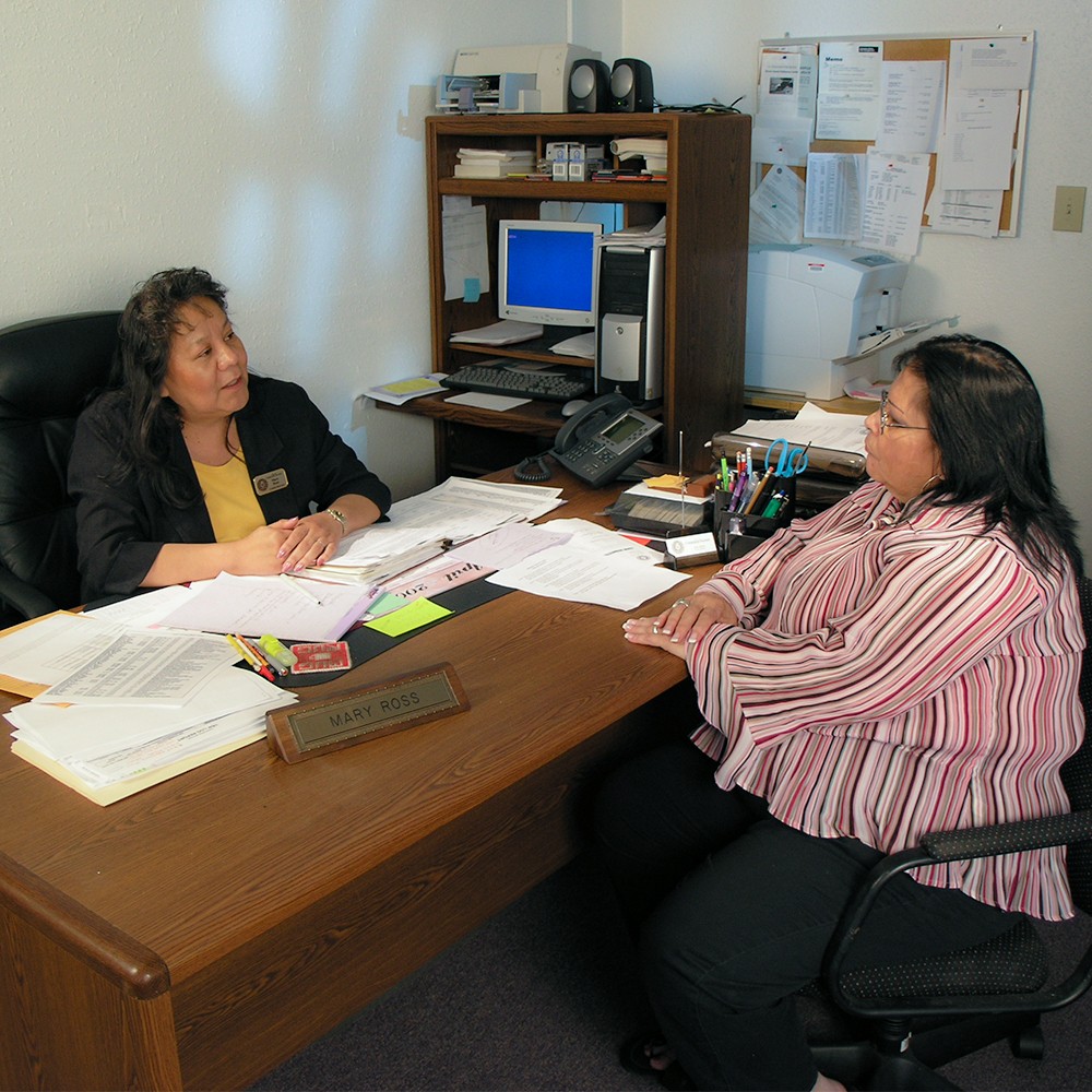A Native American Counselor sitting at her desk with a Native American woman across from her.