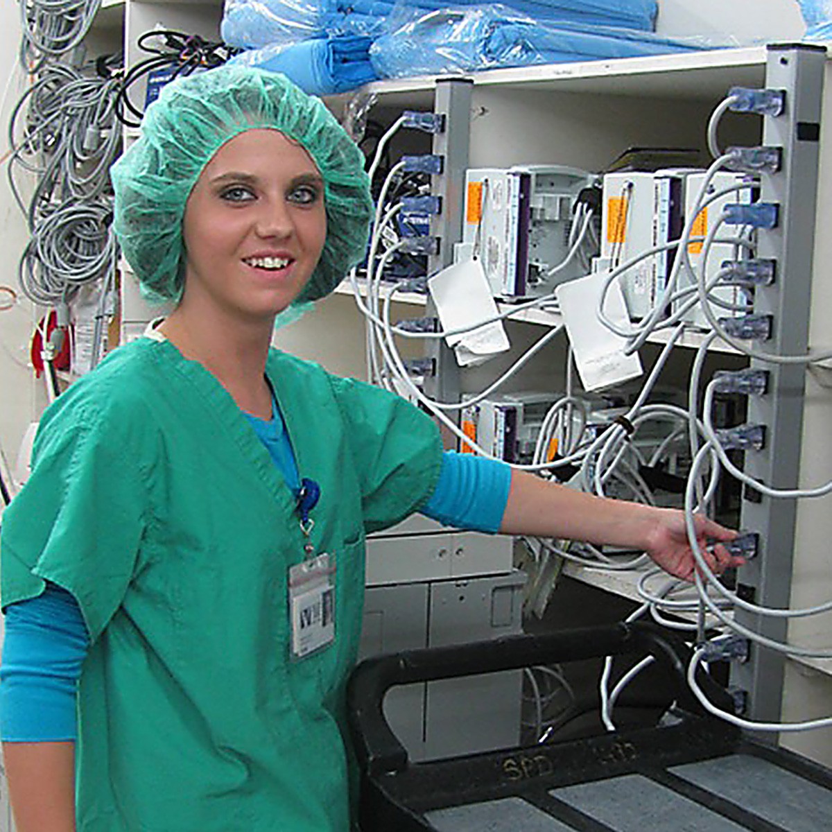 Smiling woman wearing medical scrubs and cap plugs in equipment.