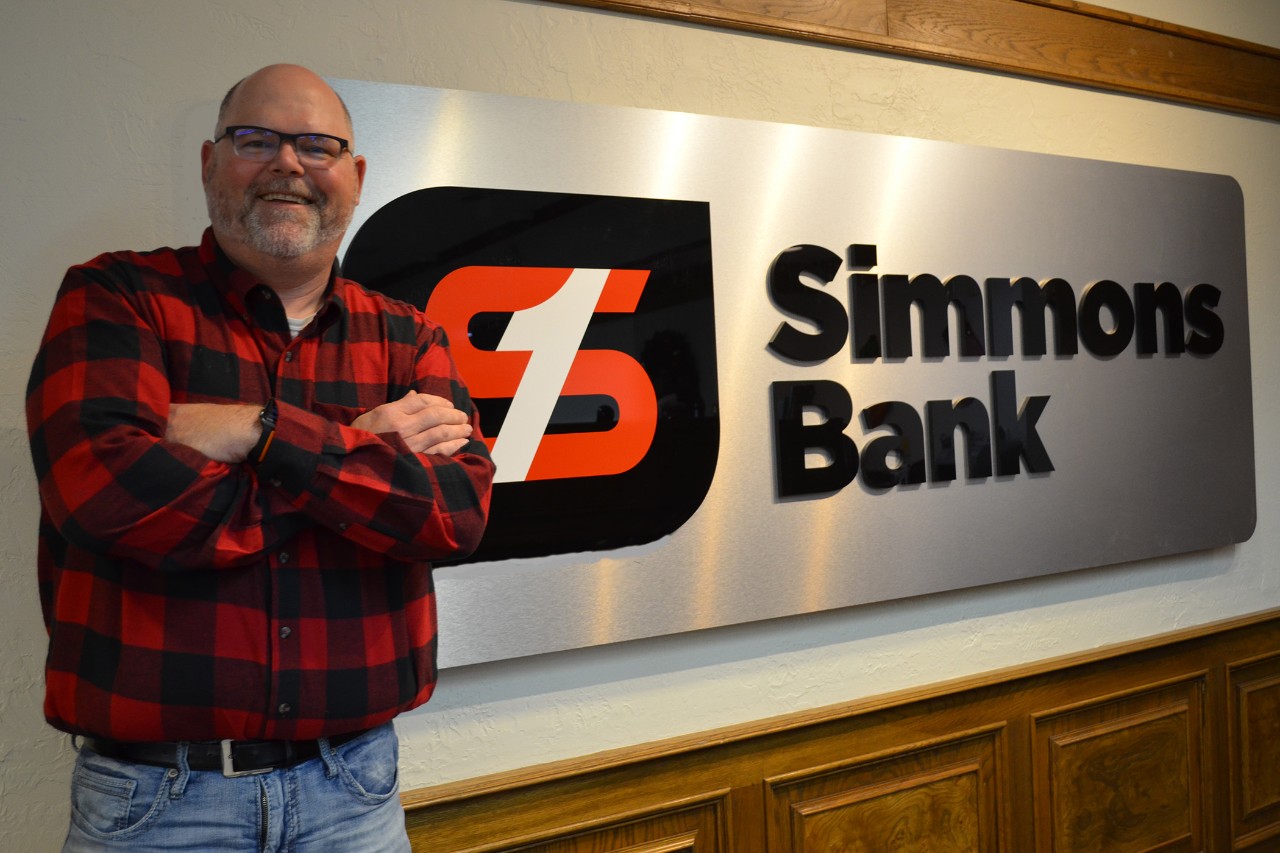 Smiling man with arms crossed in front of Simmons Bank sign.