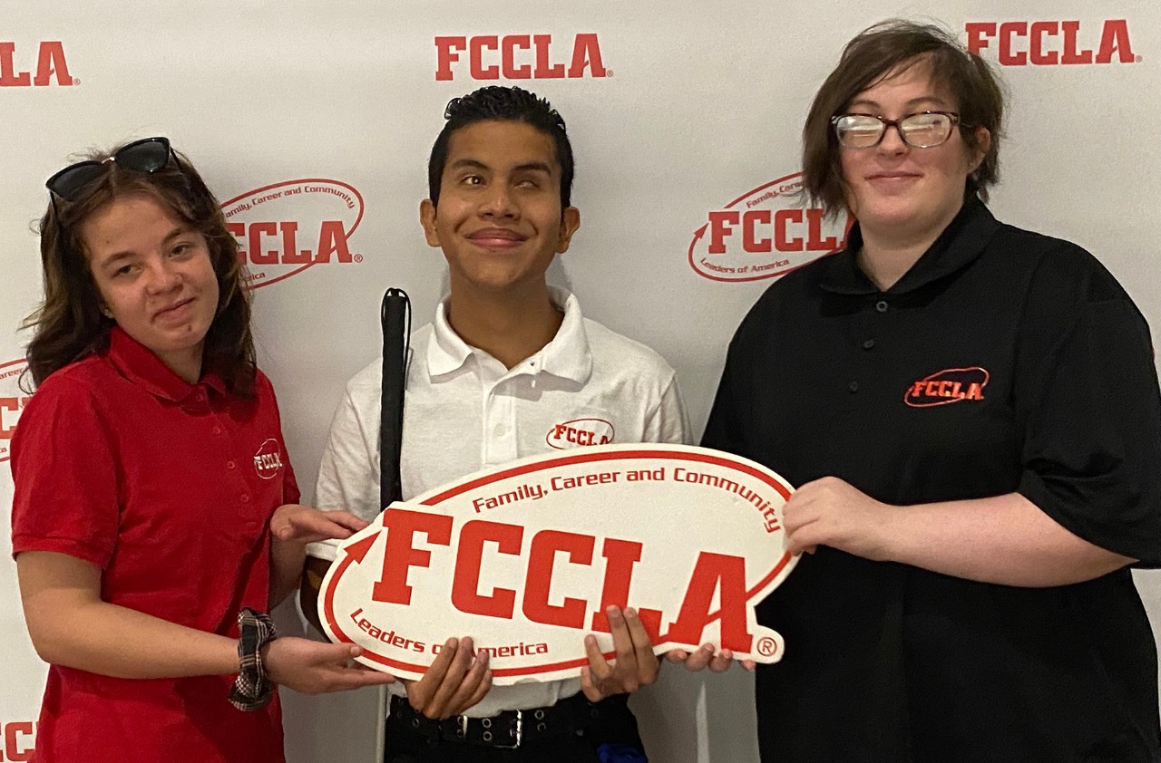 3 smiling young people hold sign with FCCLA logo.