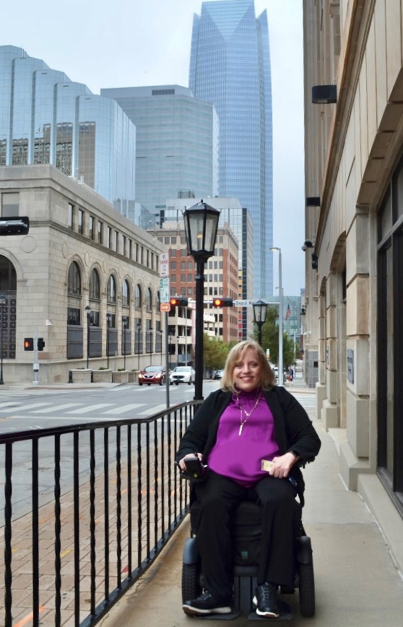 Smiling woman in wheelchair on downtown street.