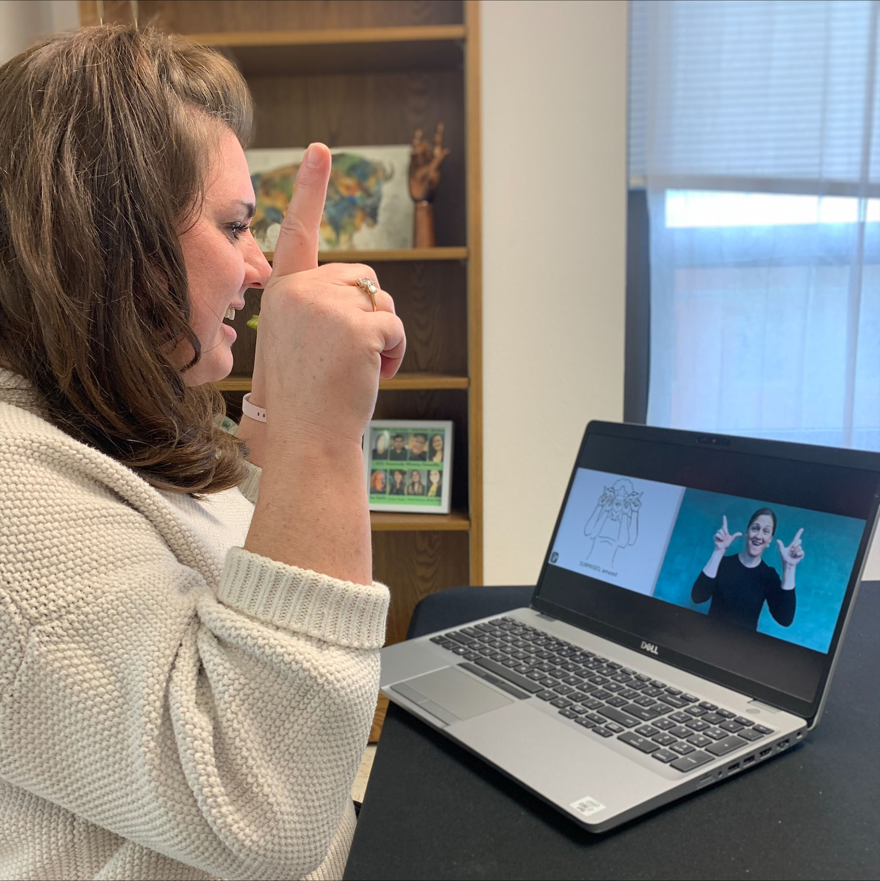 Woman signs as she watches video training on laptop